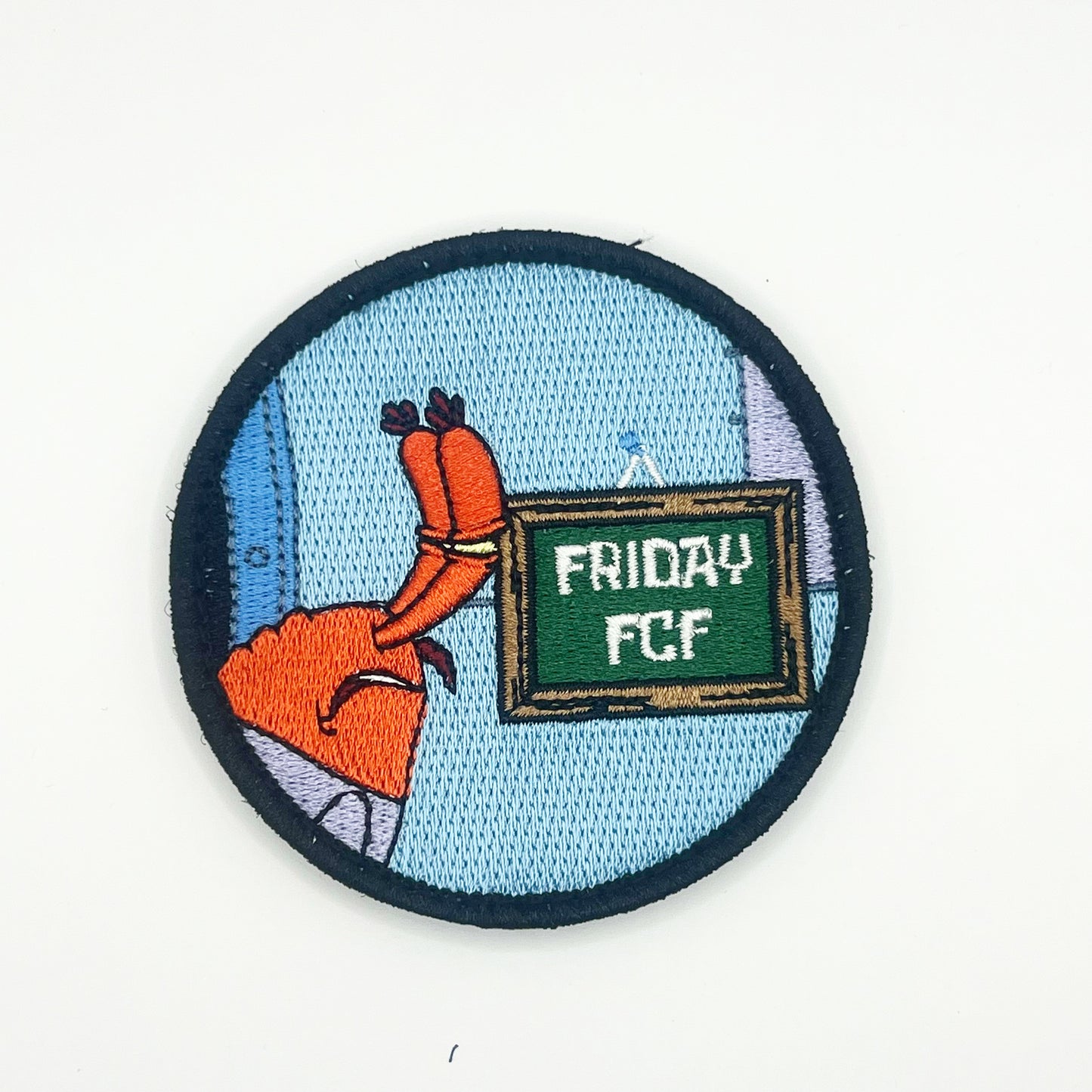 A round patch featuring an animated crab character with a sign that reads 'Friday FCF'. The background is blue, and the patch has an embroidered edge.