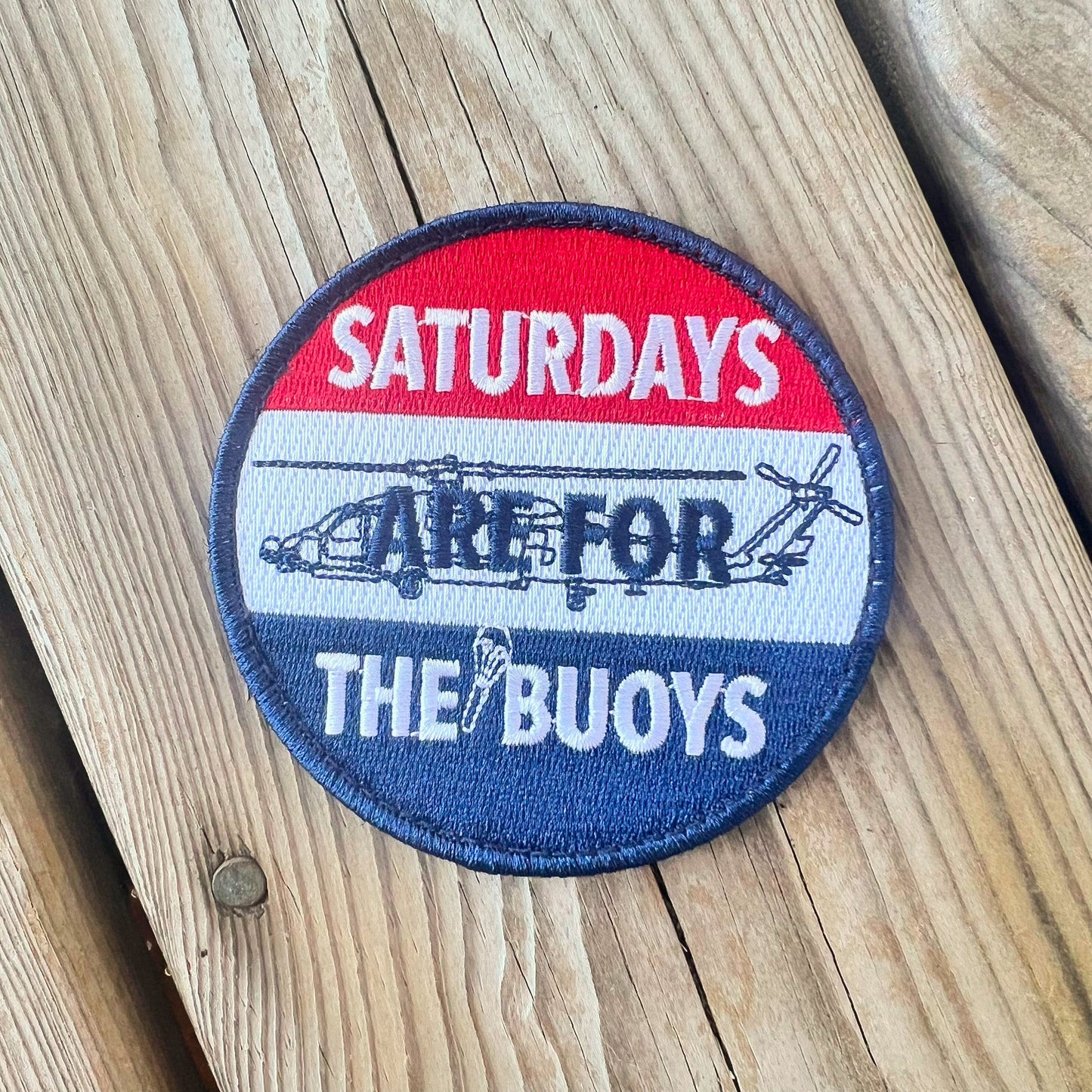 A round patch with a blue background featuring a red and white design and the text 'Saturdays are for the Buoys' along with an image of a helicopter.